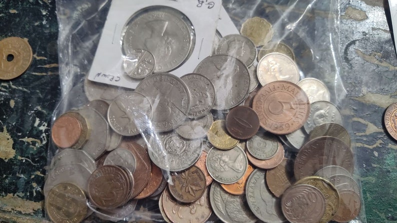 May include: A clear plastic bag filled with a variety of coins. The coins are of different sizes, shapes, and colors, including silver, copper, and bronze. Some coins are partially visible, while others are stacked on top of each other.