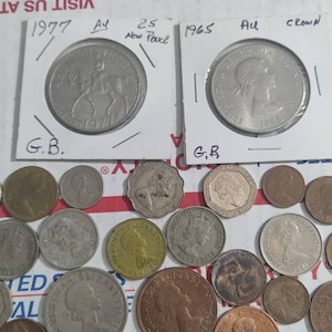 May include: A collection of various coins, including British coins from 1977 and 1965, displayed in protective sleeves. The coins feature portraits and equestrian designs. A variety of other coins are scattered around.