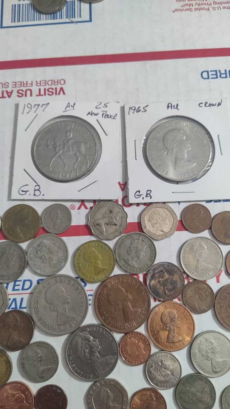 May include: A collection of various coins, including British coins from 1977 and 1965, displayed in protective sleeves. The coins feature portraits and equestrian designs. A variety of other coins are scattered around.