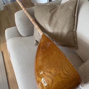 May include: A traditional stringed instrument with a long neck and a pear-shaped body. The instrument has a polished, glossy finish, highlighting the wood's grain. The neck is slender, with frets. The headstock has tuning pegs.
