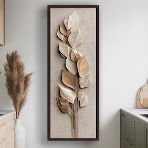 May include: A framed wall art piece featuring a stylized botanical design. The artwork showcases a cluster of layered leaves in shades of beige, cream, and brown, set against a textured, neutral background. The frame is a dark brown, adding contrast to the artwork.