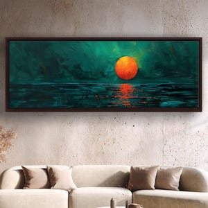 May include: An abstract landscape painting in a dark wooden frame. The artwork shows a bright orange sun reflecting on teal water, set against a teal and green background. The painting hangs above a cream sofa and a white coffee table.