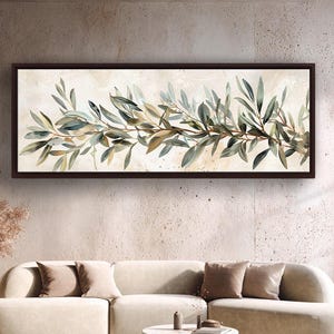 May include: A rectangular framed artwork depicting olive branches with green and brown leaves in watercolour. The artwork is set against a cream background and is displayed above a cream sofa and round coffee table.