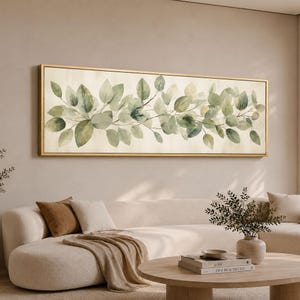 Peut inclure: Une œuvre d'art murale rectangulaire horizontale représentant une peinture à l'aquarelle de feuilles d'eucalyptus vertes sur un fond crème, encadrée par un cadre doré fin. L'œuvre montre une branche de feuillage continue sur la toile.