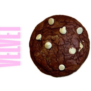 Puede incluir: Una galleta de terciopelo rojo con chispas de chocolate blanco. La galleta es redonda y tiene una superficie ligeramente agrietada.