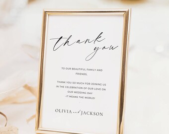 May include: A gold framed sign with the words "thank you" in elegant script. The sign includes a message to family and friends, thanking them for joining in the celebration of love on their wedding day. Names Olivia and Jackson are at the bottom.