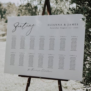 以下が含まれることがあります： 木製のイーゼルに立てられた白いウェディング席次表。 「Elianna & James」の名前と「2023年8月12日土曜日」の日付が記載されています。ゲストの名前は、テーブル番号ごとに列に表示されています。