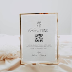 May include: A gold-framed sign with the words "House Fund" in elegant script, accompanied by a QR code and a message. The sign is on a white background, with the names "Ava & James" at the bottom.