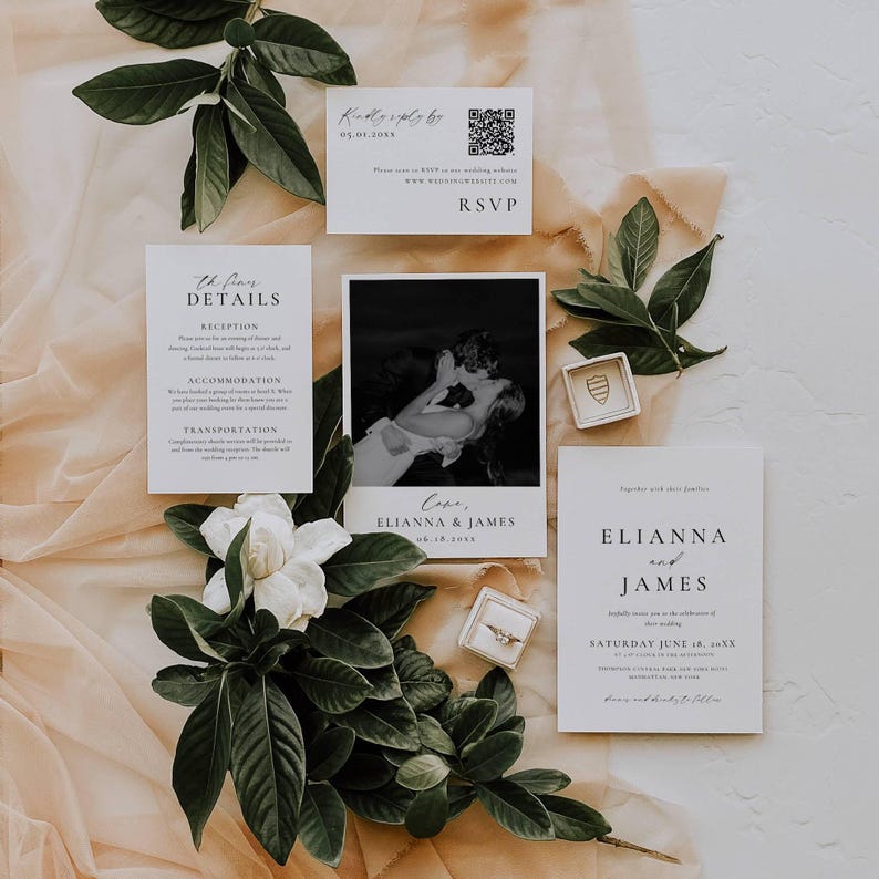 May include: Wedding invitation suite with a black and white photo, RSVP card, and details card. The suite includes a photo of a couple kissing, and the names ELIANNA and JAMES are printed on the cards. Green leaves and a white flower are arranged around the cards.
