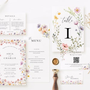 May include: Wedding invitation suite with floral designs. The invitation features a watercolor wreath of pink, purple, and yellow flowers with the names "Aria and Charlie" in the center. The RSVP card has a QR code and the text "Please scan for more details and to RSVP to our wedding website: www.weddingwebsite.com".