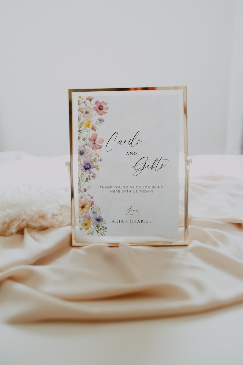 May include: A white sign with a gold frame and floral border. The sign reads "Cards and Gifts" with the text "Thank you so much for being here with us today! Love, Aria + Charlie" below.