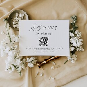 May include: A white RSVP card with the text "Kindly RSVP" and a QR code, surrounded by white flowers and a gold wax seal. The card also includes the date "By 06.11.25" and website information. The background is a beige fabric.