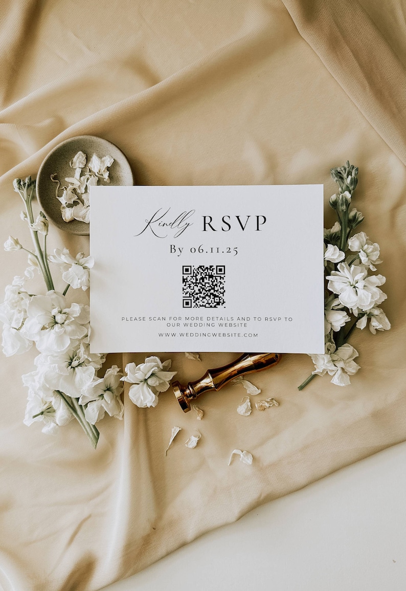 May include: A white RSVP card with the text "Kindly RSVP" and a QR code, surrounded by white flowers and a gold wax seal. The card also includes the date "By 06.11.25" and website information. The background is a beige fabric.