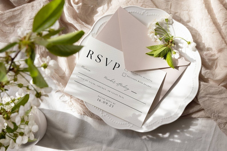 May include: A white RSVP card with a black border and the text "RSVP" in large, bold letters. The card has a section for the guest's name, a checkbox for accepting or declining the invitation, and a line for the number of guests attending. The card also includes the text "Choice of Steak, Chicken, or Vegan Meal" and "Please reply by 16.09.23". The card is on a white plate with a pink envelope and a sprig of white flowers.