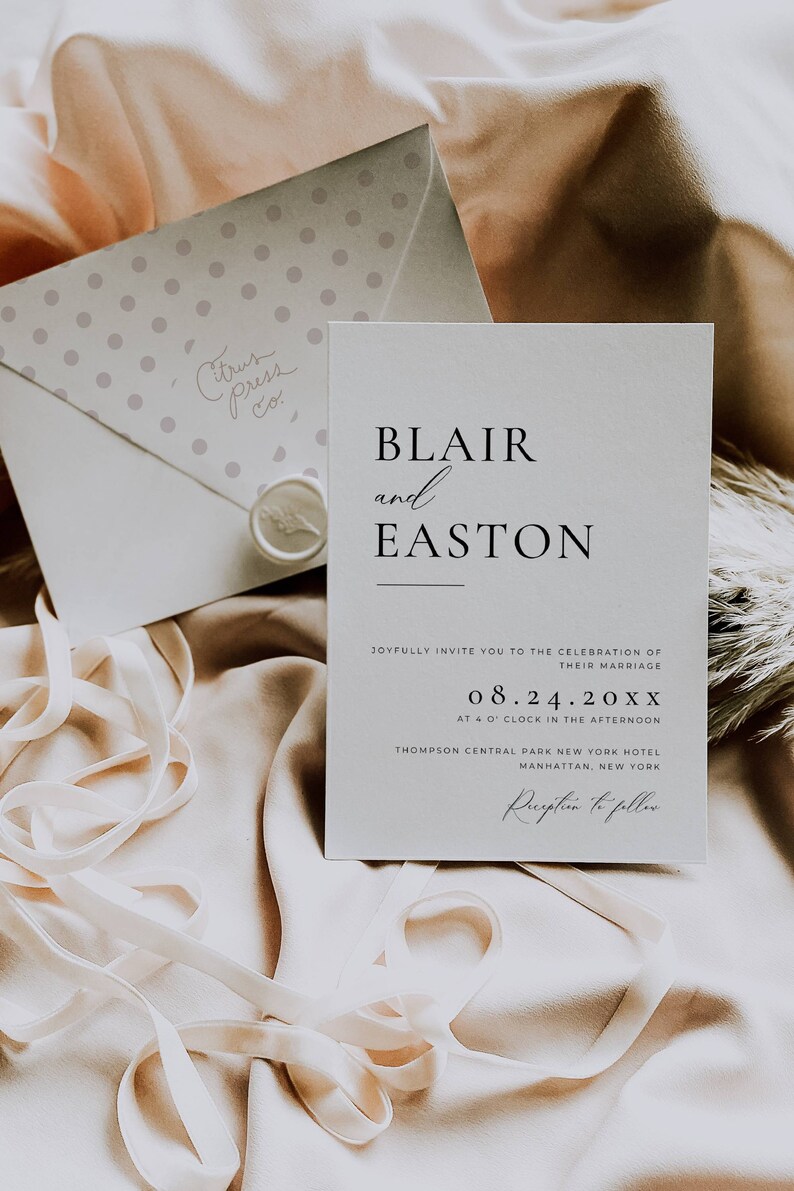 May include: A wedding invitation with the names "Blair and Easton" in elegant black font. The invitation includes the date, time, and location of the ceremony. An envelope with polka dots and the text "Citrus Press Co." is also visible, along with a ribbon.