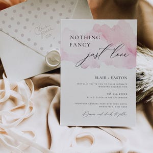 May include: A wedding invitation with the words "Nothing Fancy Just Love" in elegant script. The invitation has a watercolor-style pink design and includes the names Blair and Easton, along with the wedding date and location.