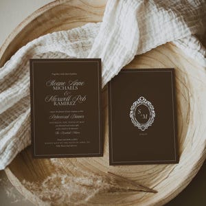 May include: Two rectangular dark brown cards with white text and borders. The left card features wedding rehearsal dinner details for Sloane Anne Michaels and Maxwell Rob Ramirez. The right card displays an ornate oval frame with the initials S & M.
