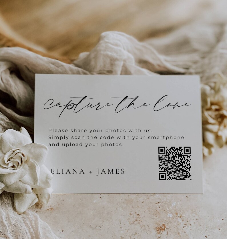 May include: White card with black text that reads "Capture the Cove". Below the text is a QR code and the text "Please share your photos with us. Simply scan the code with your smartphone and upload your photos. ELIANA + JAMES".