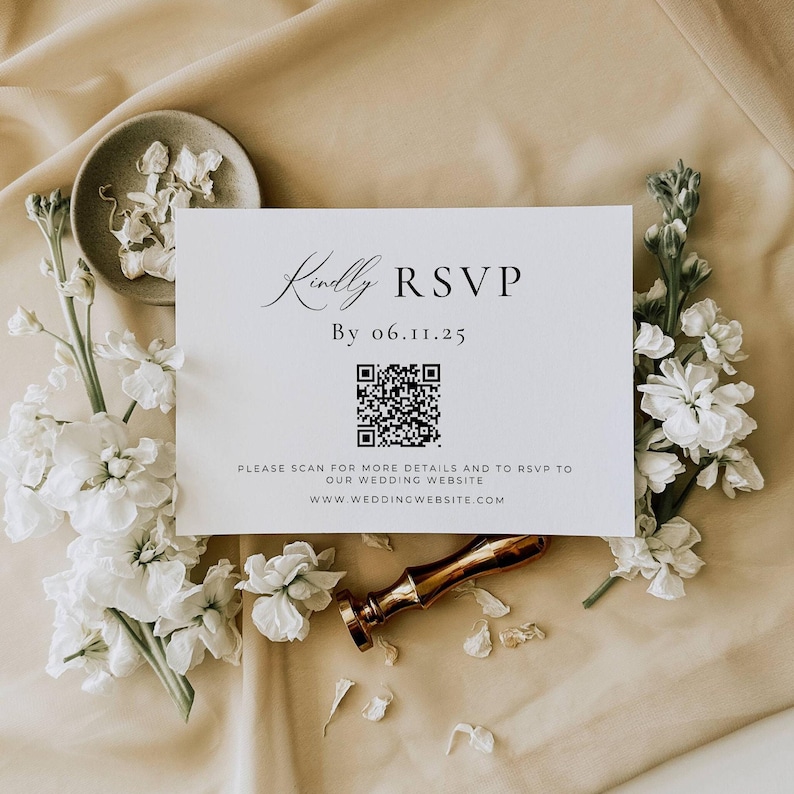 Peut inclure: Une carte RSVP blanche avec une calligraphie &eacute;l&eacute;gante, un code QR et le texte "Kindly RSVP By 06.11.25." La carte est entour&eacute;e de fleurs blanches et d'un sceau de cire dor&eacute;, sur un fond beige. Le site web est www.weddingwebsite.com.