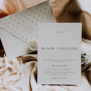 May include: A white wedding invitation with a simple design. The invitation features the names "Blair and Easton" and the date "08.24.20XX". The invitation also includes the location of the wedding, which is the Thompson Central Park New York Hotel in Manhattan, New York.