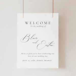 May include: A white wedding welcome sign with black text. The sign reads "WELCOME To the wedding of Blair and Easton." Additional text includes "We're so glad you're here celebrating our love on our wedding day" and the date and location.