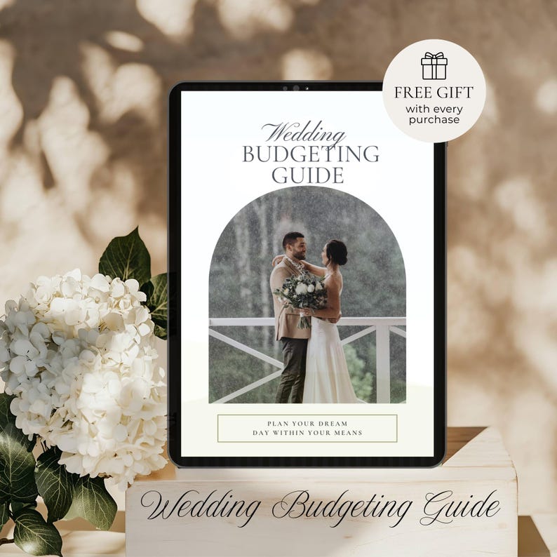 May include: A digital tablet displays a wedding budgeting guide with a photo of a couple. The text reads "Wedding Budgeting Guide" and "Plan Your Dream Day Within Your Means." A "Free Gift" offer is also shown. White flowers and a wooden block are in the foreground.