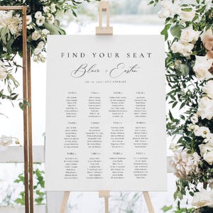 Op de afbeelding: Een wit bruiloftstafelplan op een houten ezel met de tekst FIND YOUR SEAT, de namen Blair + Easton, de datum 08.24.2025 en de locatie LOS ANGELES, gevolgd door een lijst met gastennamen georganiseerd per tafelnummer van 1 tot en met 12.