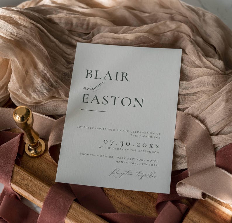 May include: A wedding invitation with the names "Blair and Easton" printed in black on a light gray card. The invitation includes the date, time, and location of the ceremony. A gold wax seal and ribbons are in the background.