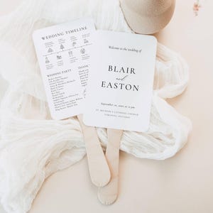 Könnte beinhalten: Zwei weiße Hochzeitsfächer mit Holzgriffen. Ein Fächer zeigt einen Hochzeitszeitplan und Party-Details. Der andere Fächer lautet "Willkommen zur Hochzeit von Blair und Easton" mit Datum und Ort.