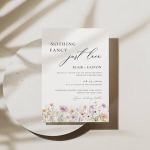 May include: Wedding invitation with a floral design. The text reads "Nothing Fancy just love" and includes the names Blair + Easton, the date 08.24.20XX, and the location Thompson Central Park New York Hotel, Manhattan, New York.