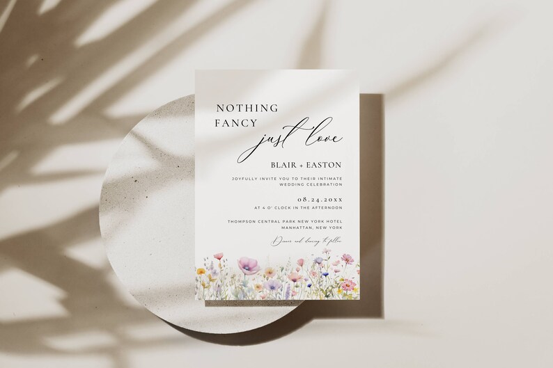 May include: Wedding invitation with a floral design. The text reads "Nothing Fancy just love" and includes the names Blair + Easton, the date 08.24.20XX, and the location Thompson Central Park New York Hotel, Manhattan, New York.