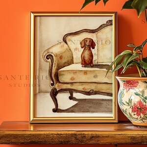 Op de afbeelding: Een ingelijste aquarel van een teckel op een antieke fauteuil met bloemenpatroon. Het kunstwerk zit in een gouden lijst tegen een oranje muur. De tekst "SANTE RIO STUDIOS" is zichtbaar. Thema: dierenkunst.