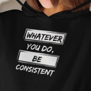 Könnte beinhalten: Schwarzer Kapuzenpullover mit dem Text "WHATEVER YOU DO, BE CONSISTENT" in weißer, umrandeter Schrift. Der Text ist in drei Zeilen in rechteckigen Kästen angeordnet. Der Hoodie hat eine Kapuze mit Kordelzug.