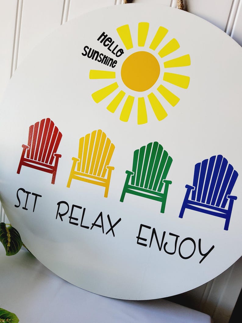 K&ouml;nnte beinhalten: Runder wei&szlig;er Anh&auml;nger mit gelber Sonne und der Aufschrift "Hello Sunshine". Darunter vier farbige Adirondack-St&uuml;hle in Rot, Gelb, Gr&uuml;n und Blau mit den Worten "SIT RELAX ENJOY" in Schwarz.