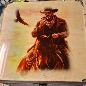 May include: A wooden box with a cowboy riding a horse, smoking a cigar, and an eagle in flight. The image is a sepia-toned illustration with a glossy finish and decorative corner accents.