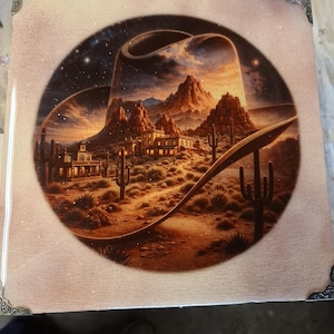 May include: A square decorative tile featuring a detailed illustration of a cowboy hat framing a desert landscape with mountains, cacti, and buildings under a starry sky. The tile has decorative corner accents.