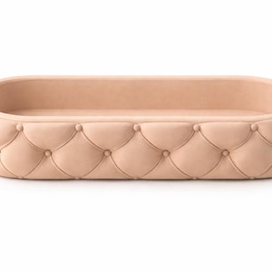 Puede incluir: Una cama para mascotas de forma ovalada y color melocotón claro, con un diseño acolchado. La cama tiene un perfil bajo con un interior acolchado y un exterior con botones. El diseño es simple y elegante, adecuado para un perro o gato pequeño.