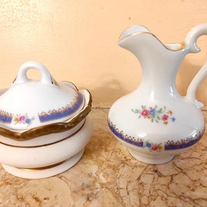 May include: A white porcelain creamer and sugar bowl set with a blue and gold trim and floral design.