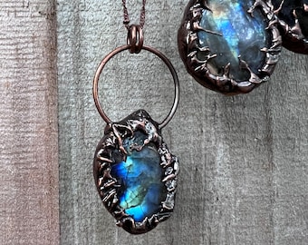 Puede incluir: Dos colgantes envueltos en alambre de cobre con piedras de labradorita azul iridiscente. Los colgantes cuelgan de cadenas de cobre.