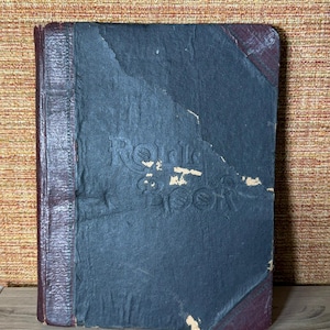 May include: An antique book with a dark blue cover and burgundy leather spine and corners. The title "Rold's Book" is embossed on the cover. The book shows signs of wear and tear, suggesting it is vintage.