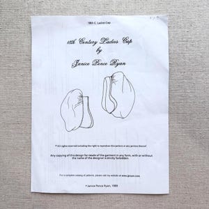 May include: A white paper with text and illustrations of a cap. The text reads "18th Century Ladies Cap by Janice Pence Ryan." The paper also includes copyright information and the designer's website.