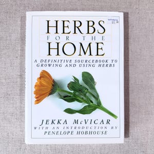 May include: A book titled "HERBS FOR THE HOME" with an orange flower and green leaves on the cover. The book is a definitive sourcebook to growing and using herbs, written by Jekka McVicar.
