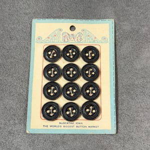 May include: A vintage card of twelve black buttons with a textured design and gold-colored accents. The buttons are arranged in three rows of four on a light blue card. The card has the text "Muscatine, Iowa" and "The World's Biggest Button Market."