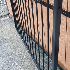May include: Black metal fence panel with vertical bars and rounded finials. The panel is attached to a brown wooden fence.