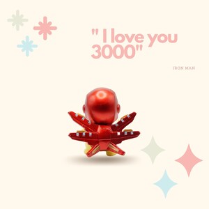 May include: A red and gold Iron Man figurine with the text "I love you 3000" in pink letters. The figurine is facing away from the camera and has its arms outstretched.