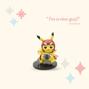 May include: A yellow Pikachu figurine wearing a red and black Spiderman costume with gold web accents. The figurine is standing on a black base and the text "I'm a nice guy!" is written in pink above the figurine. The text "SPIDERMAN" is written in black below the figurine.