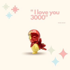 May include: A small, yellow Iron Man figurine wearing a red and gold suit. The figurine is standing with its back to the viewer and has its arms outstretched. The text "I love you 3000" is written in pink letters on a white background. The words "Iron Man" are written in black letters below the text.