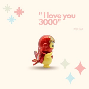May include: A yellow Pikachu figurine wearing a red and gold Iron Man suit. The figurine is standing on a white background with the text "I love you 3000" and "IRON MAN" written below.