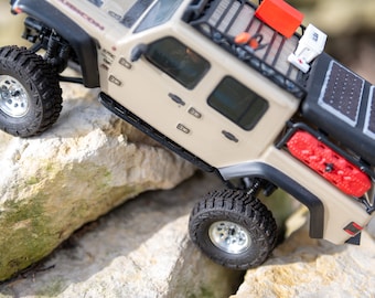 Pode incluir: Um Jeep Wrangler bege com um rack de teto preto e um painel solar na parte de trás. O Jeep está dirigindo sobre rochas.