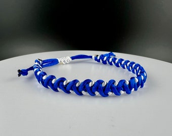 May include: A blue and white braided friendship bracelet. The bracelet is made with two strands of cord, one blue and one white, that are woven together in a complex pattern.